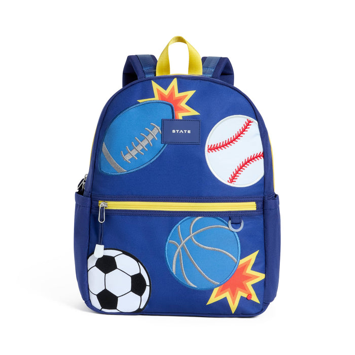 A royal blue backpack decorated with sports-themed graphics including a football, baseball, basketball, soccer ball, and starburst shapes, with a yellow top handle and zipper trim. Front view on a plain white background.