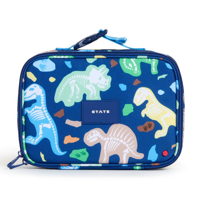 A rectangular blue lunch bag with a dinosaur skeleton print, featuring a blue top handle and a central blue brand patch that reads 'STATE'.