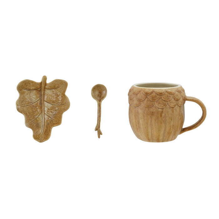 Three-piece ceramic coffee mug set in a light brown reactive glaze finish, featuring a leaf-shaped saucer, a small spoon, and a mug with a textured acorn pattern.