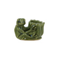A small green glazed stoneware figurine shaped like a seated frog holding a lotus flower, photographed on a plain white background.