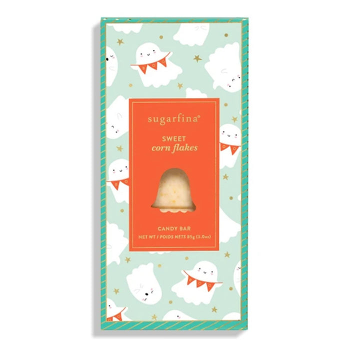 A packaged candy bar in a tall rectangular box with a mint green and orange design, printed with white cartoon ghosts and gold stars. The center label reads 'sugarfina' and 'sweet corn flakes' with a clear window showing a single corn-flake candy bar inside.