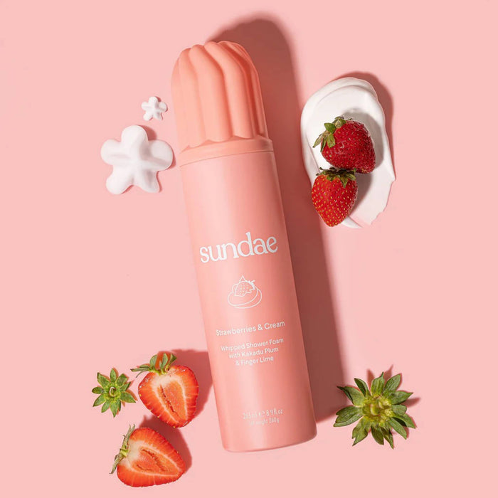 Sundae Strawberries and Cream scented whipped shower foam in pink bottle, with strawberries and whipped cream, on a pink background.