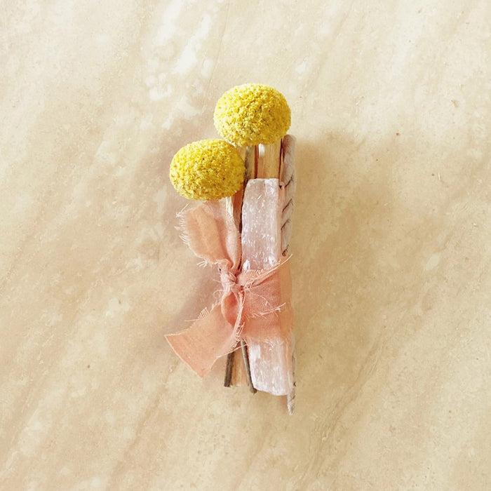 Sunny Side palo santo bundle with pink selenite and dried yellow craspedia flowers bundled in vintage peach colored ribbon.