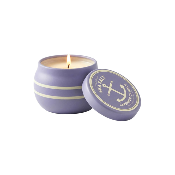 Purple tin candle with a lit wick and matching lid on a white background.