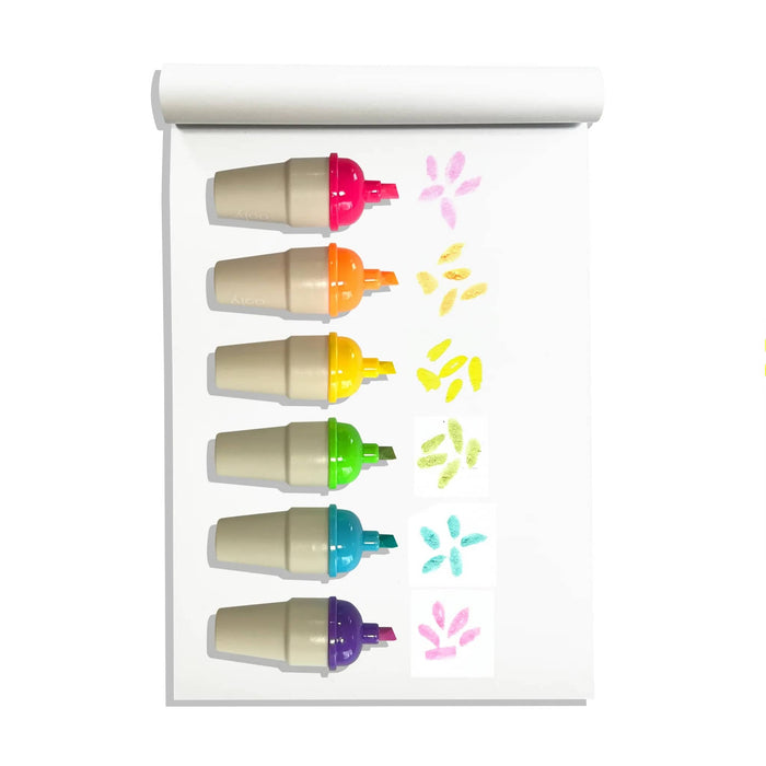 Six ice cream cone-shaped highlighters in different colors (pink, orange, yellow, green, blue, purple), caps off, with simple marks on a white sheet of paper to show ink color, on a white background.