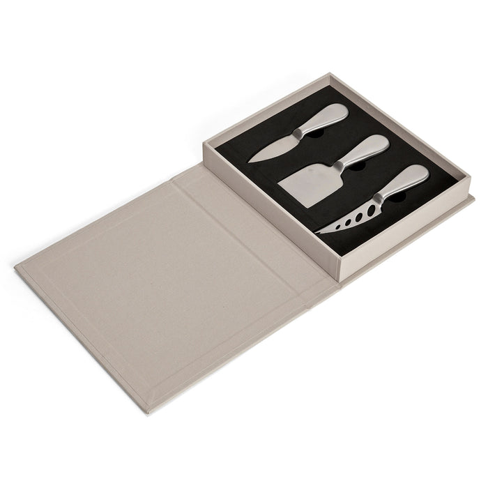 Printworks The Essentials Cheese Tools for Cheese Lovers, set of 3 stainless steel cheese knives in beige book box packaging, open to show knives inside resting on a black background.