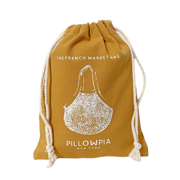 A mustard yellow canvas drawstring pouch with a white printed illustration of a pillow and the text 'THE FRENCH MARKET BAG' and 'PILLOWPIA NEW YORK'.