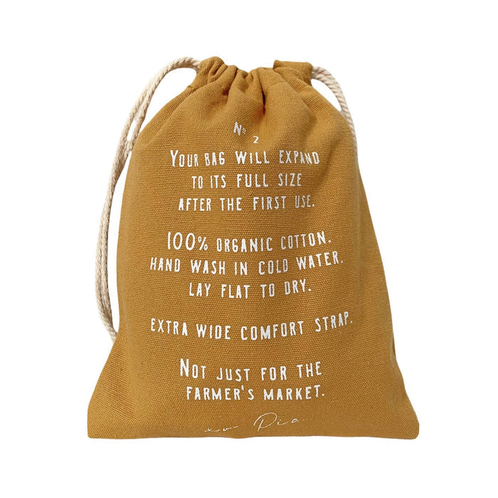 A mustard yellow cotton drawstring bag with white printed text detailing the cotton net bag care instructions, shown against a plain white background.
