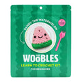Front of green pouch packaging for The Woobles Sandy the Watermelon beginner crochet kit, on a white background.