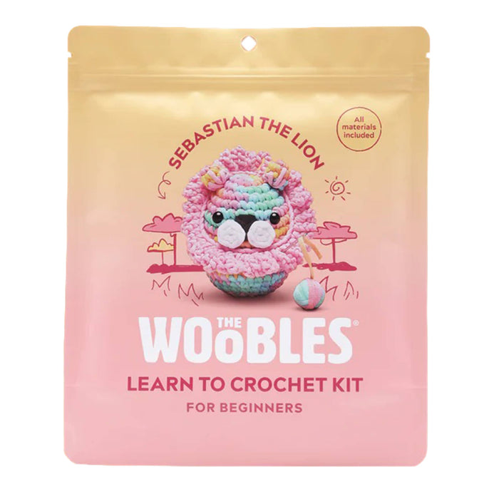 Front of pink and gold ombre pouch packaging for The Woobles Pastel Sebastian the Lion beginner crochet kit, on a white background.