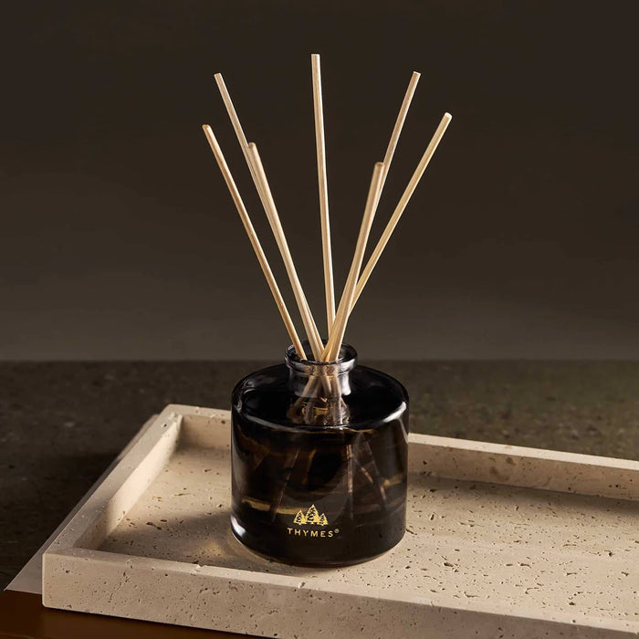 Black and white marbled glass diffuser with wooden reeds, on a stone surface.