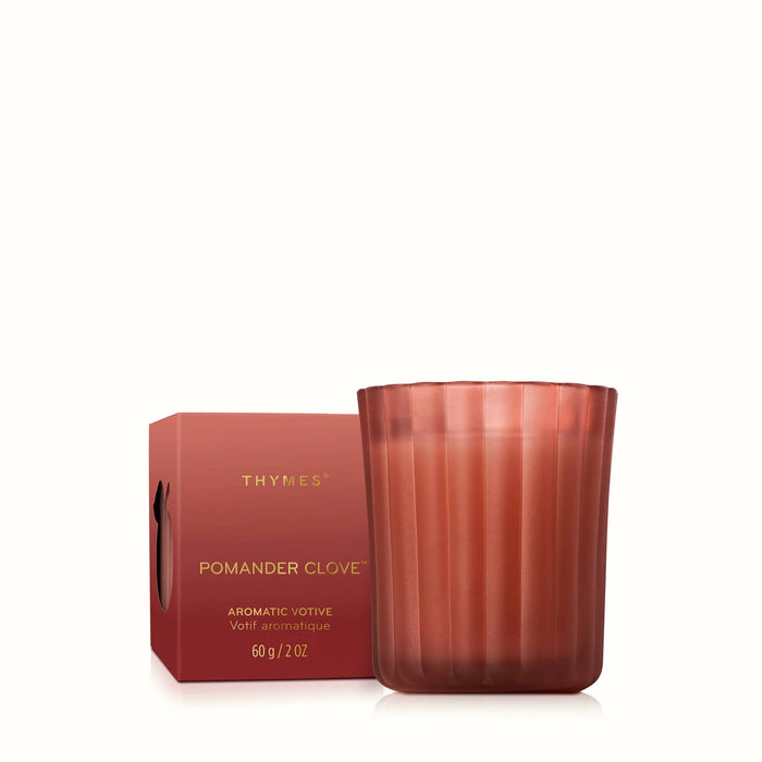 A Thymes Pomander Clove scented votive candle in a ribbed, translucent soft red glass vessel, shown next to its matching red ombre packaging box on a clean white background.