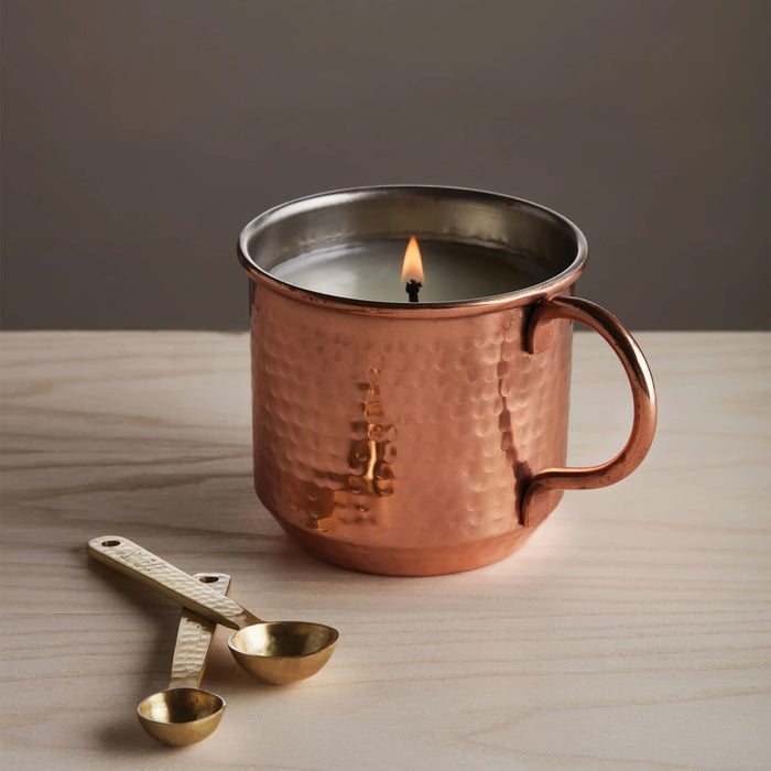Thymes 10 ounce simmered cider scented candle in metal copper mug, candle lit.