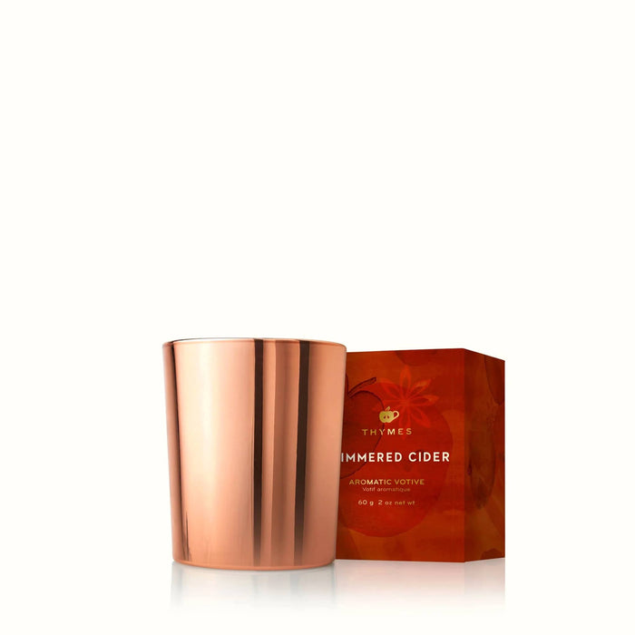 A copper-colored glass votive candle vessel with a metallic finish, shown next to its textured orange-red packaging box on a clean white background.