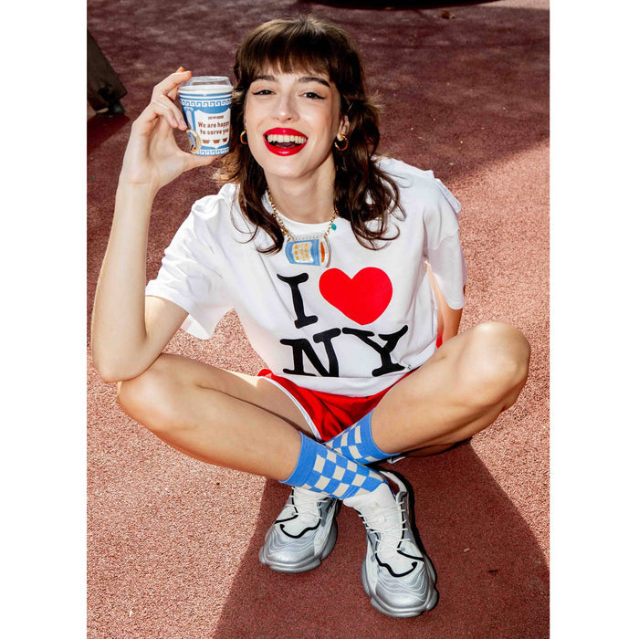 Woman sitting on a red surface wearing a 'I ❤️ NY' shirt and holding a product.