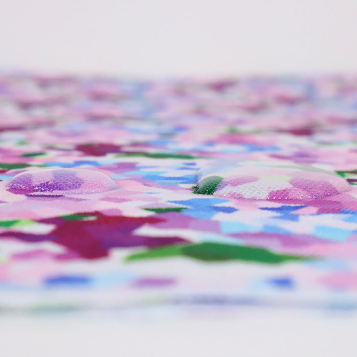 This printed WPC shows geometric shapes to resemble bunches of flowers. The colors are in an array of pinks, blues, and greens on a white background. This photo shows water droplets on the fabric.