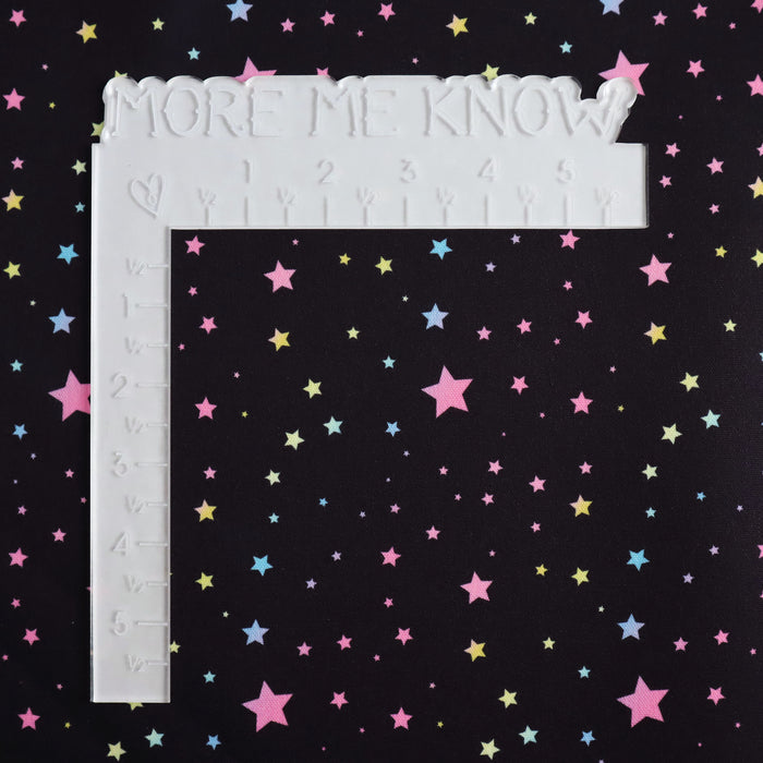 This WPCotton has pastel rainbow stars in a variety of sizes on a black background. This photo shows a white L shaped ruler for scale.