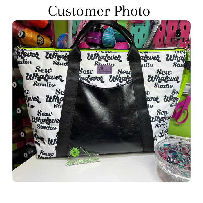 This printed WPCotton features the "Sew Whatever Studio" logo in black with multicolored spools of thread in the wording on a white background. this photo shows the fabric used for a handbag with black vinyl.