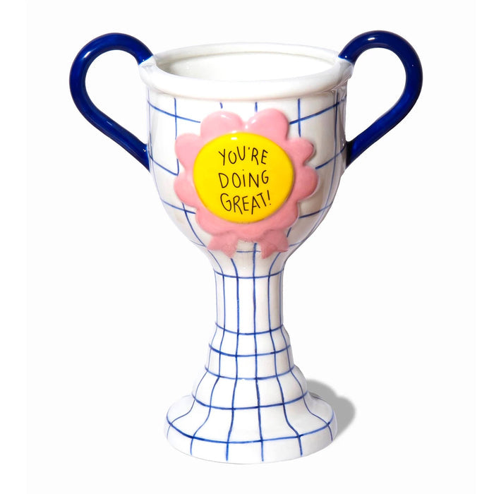 A ceramic trophy cup with dark blue handles and a blue grid pattern on a white base, featuring a pink flower rosette with a yellow circle that reads 'YOU'RE DOING GREAT!'.